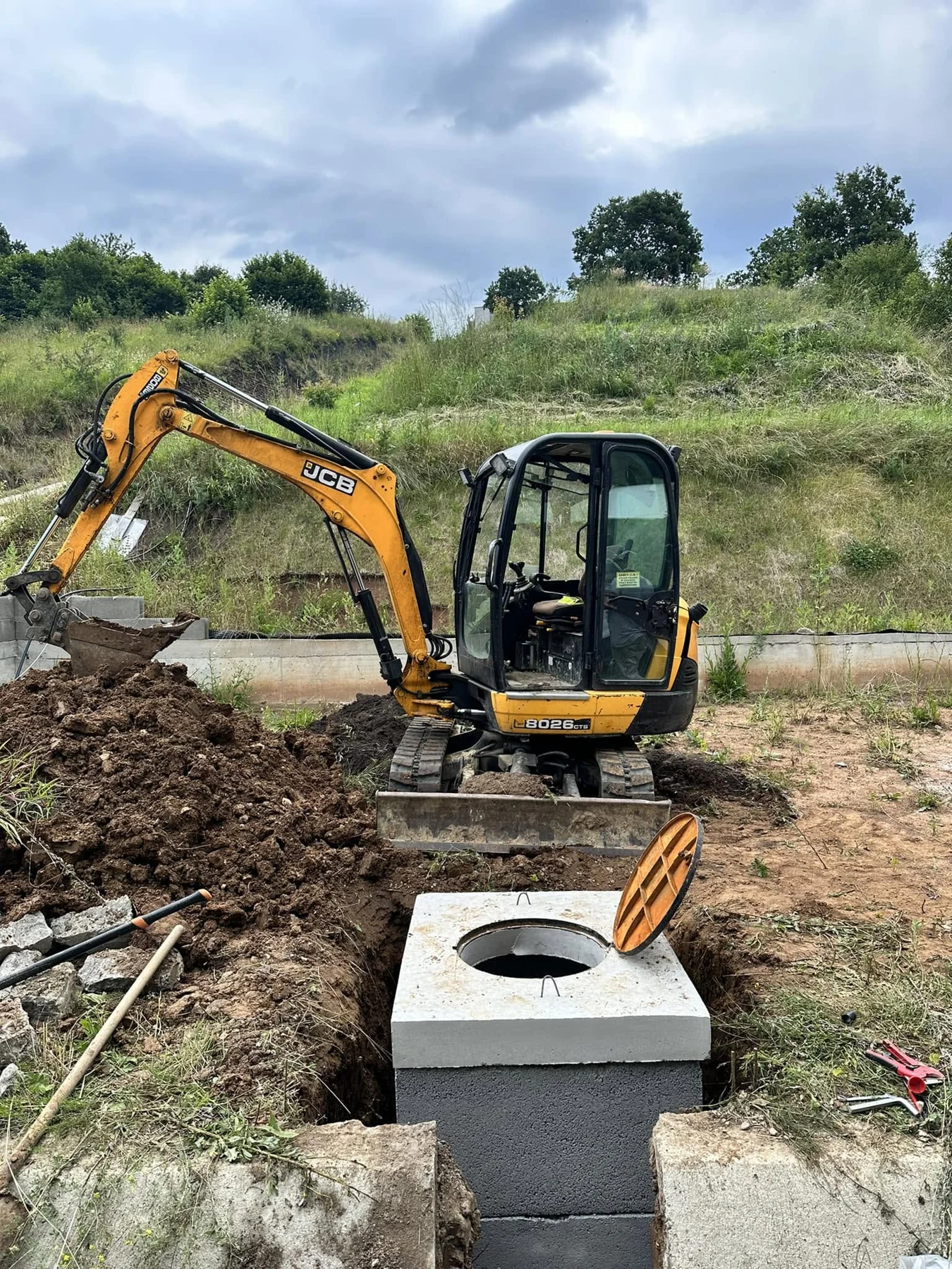 Excavator și cămin de beton pe un șantier de instalații apă-canal